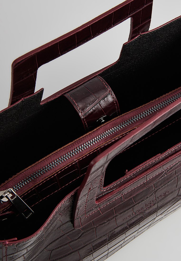 Borsa in pelle bordeaux con motivo a coccodrillo, doppi manici superiori, chiusura con zip e scomparto interno. Design strutturato e elegante.