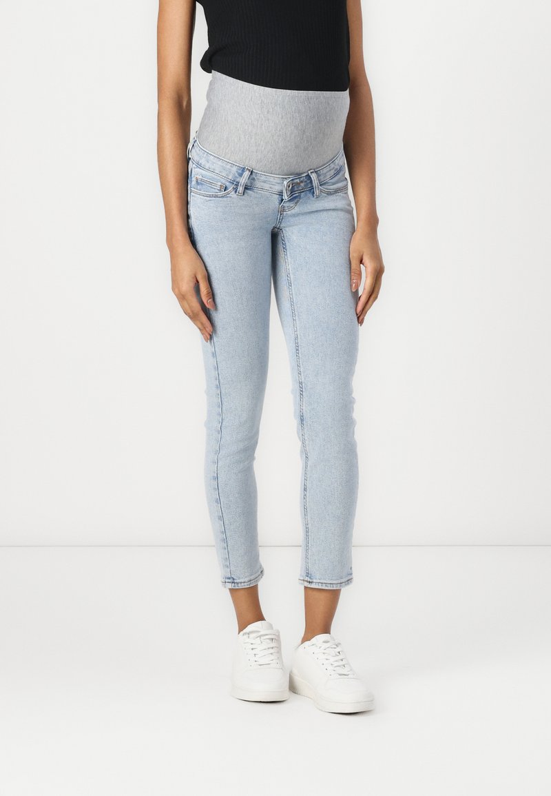 Jeans de maternidad con un acabado en denim azul claro, con un panel de barriga de jersey gris, corte ajustado y longitud recortada en el tobillo.