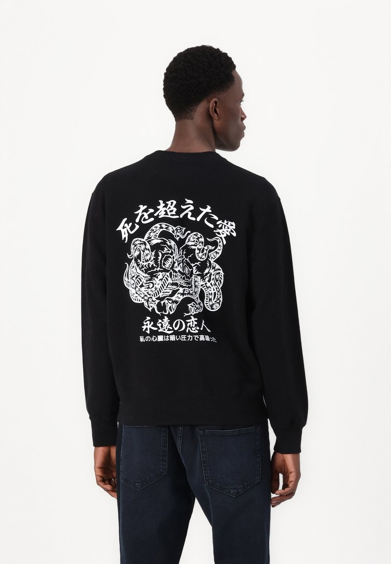 Sort sweatshirt med lange ærmer, der har et hvidt grafisk design på ryggen, som viser en drage og tekst på japansk.