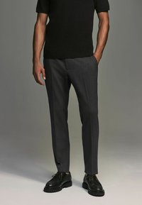 Gray tailored trousers with a smooth texture, side pockets, and a slim fit, paired with black lace-up shoes and a dark short-sleeve top.