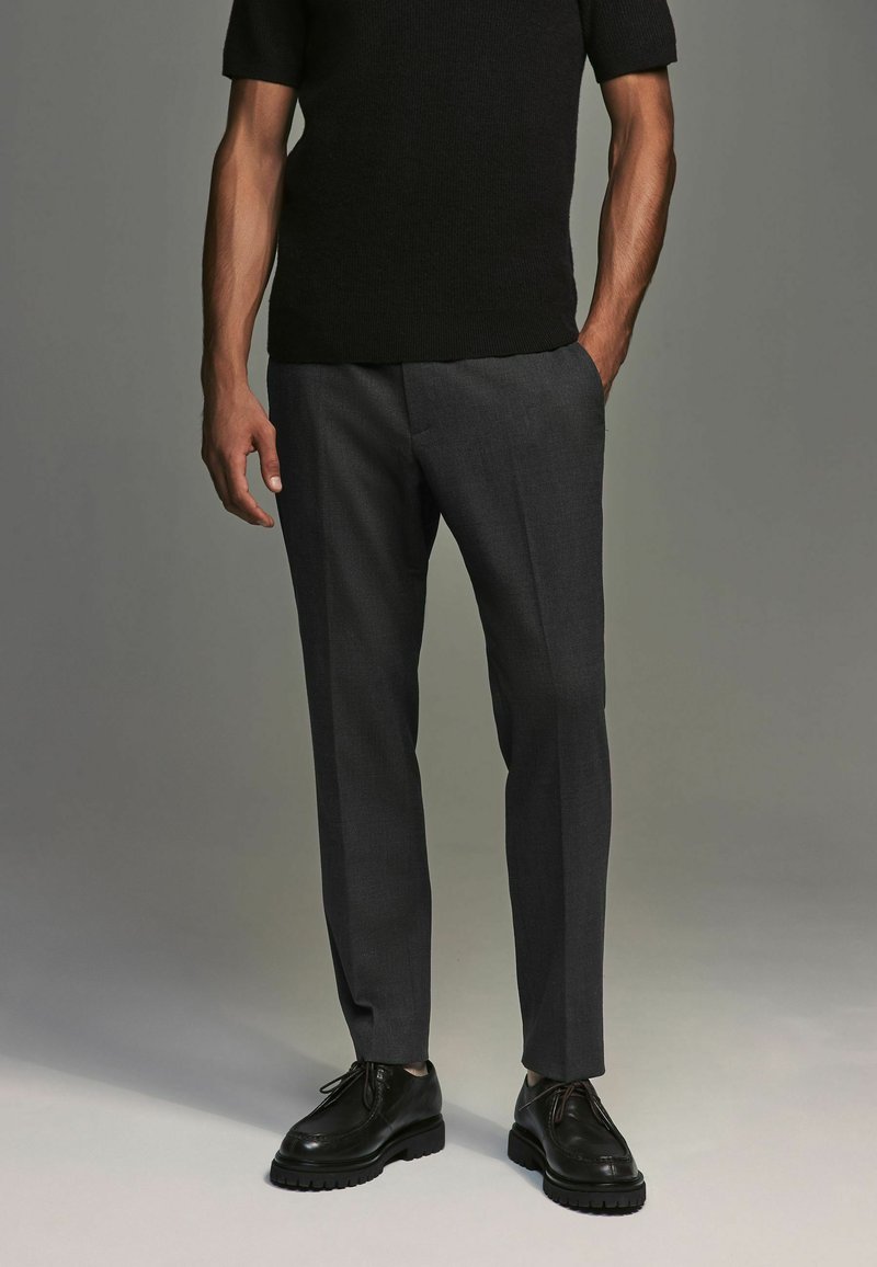 Gray tailored trousers with a smooth texture, side pockets, and a slim fit, paired with black lace-up shoes and a dark short-sleeve top.
