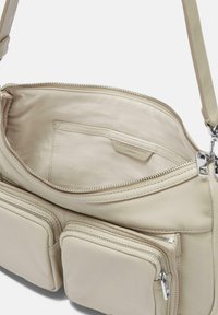 Borsa a tracolla in pelle beige con multiple tasche con zip, texture liscia e marchio discreto all'interno. L'interno presenta una tasca per l'organizzazione.