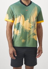 kortärmad, grön, mönstrad skjorta med gula accenter, V-ringad design, med blommönster, tillverkad av ett lätt och andningsbart tyg.