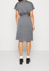 Robe à manches courtes en tissu bleu marine à motifs de formes géométriques blanches, longueur genoux, coupe décontractée. Associée à des chaussures noires à talons épais.