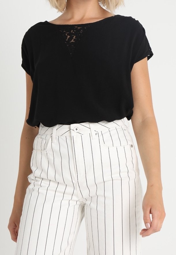 Svart kortärmad topp med spetsdetaljer vid halsringningen, matchad med högmidjade vita byxor med vertikala svarta ränder.