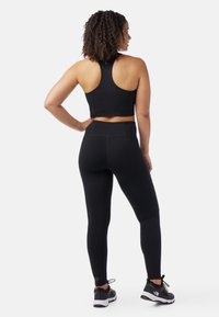 Mustat urheilulliset crop top, jossa on urheilutoppi-selkädesign, yhdistettynä korkeavyötäröisiin mustiin legginsseihin. Sujuva kangas, jossa on minimaalinen saumaus, käytössä mustat lenkkarit.