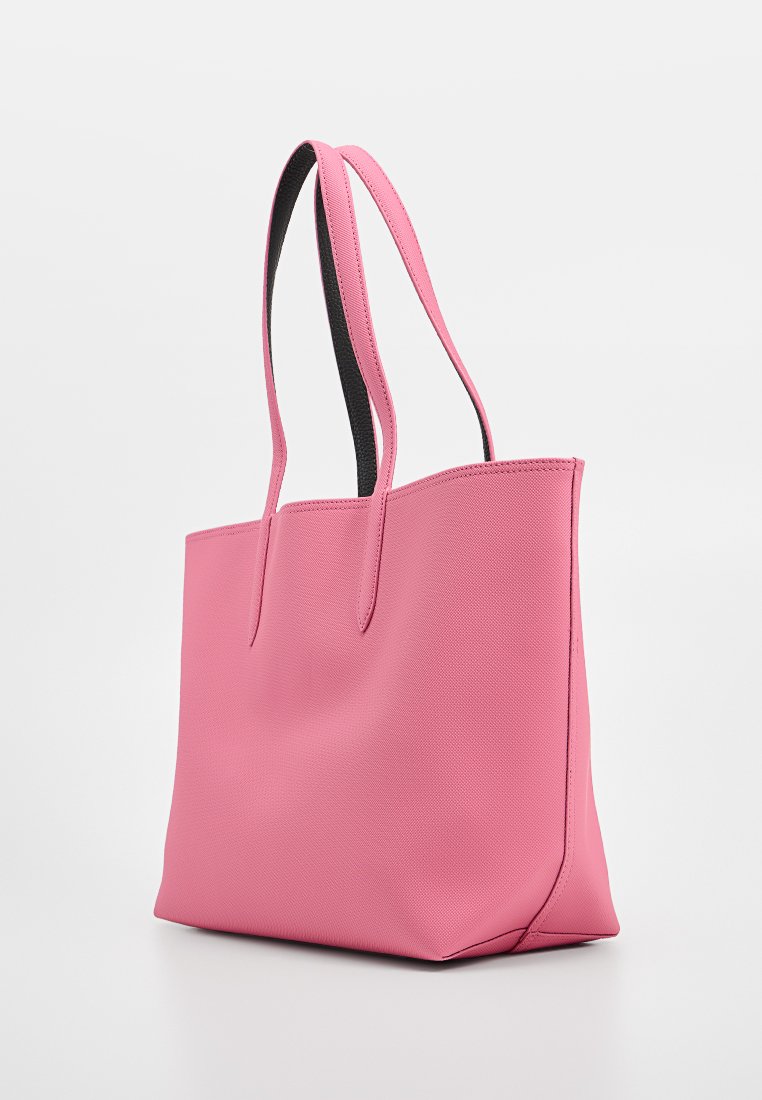 Rosa Tragetasche mit strukturiertem Oberflächen, zwei langen Griffen, offenem Oberteil und minimalistischem Design. Verfügt über schwarze Akzente in der Nähe der Griffe.