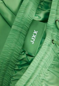 Gros plan sur une ceinture élastique verte avec une étiquette en tissu portant l'inscription "JJXX" à l'intérieur d'un short de bain ou d'un short vert.