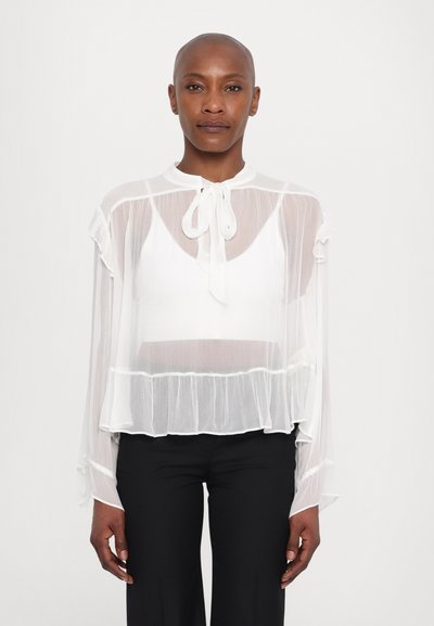 Blouse blanche en organza avec un col haut, des manches volantées et un détail noeud au cou ; design superposé sur un top blanc ; texture légère et aérienne.
