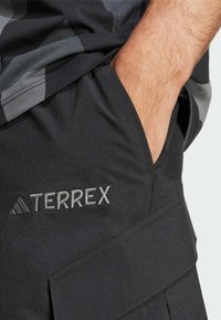 Svarta cargo-shorts med en sidficka och "TERREX"-logotyp broderad i silver. Tillverkade av lättvikts, texturerat tyg.