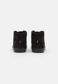 Musta niche-nahkasaappaat sileällä pinnalla, joissa on oranssi "Z" -logo takana ja musta kuminen pohja.