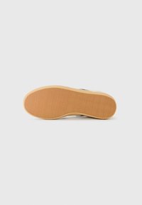 Shoe outsole with a textured, gum rubber base. Features horizontal ridges and imprints, providing traction and stability.
