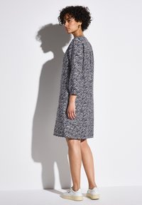 Schwarz-weiß gemustertes Kleid mit langen Ärmeln, lockerer Passform und Rundhalsausschnitt, kombiniert mit weißen Turnschuhen.