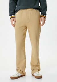 Beige sweatpants med elastisk talje, sidelommer og en afslappet pasform. Båret med hvide og beige sneakers.