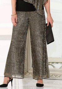 Sprankelende wijde broek in metallic zilveren stof met verticale plooien; gecombineerd met een zwarte top en clutch, aangevuld met zwarte hakken.