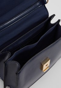 Mørkeblå læderhåndtaske med en struktureret design, guldhardware og flere indvendige rum, herunder en lynlåslomme.