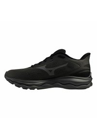 Zapatilla deportiva negra con parte superior de malla, acentos texturizados y un diseño de suela ondulada. Presenta cordones planos y un logotipo en el lado.