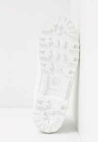 Suola di sneaker in gomma bianca con motivi di presa testurizzati, accenti in rilievo e un logo circolare con la lettera "S" per Superga.