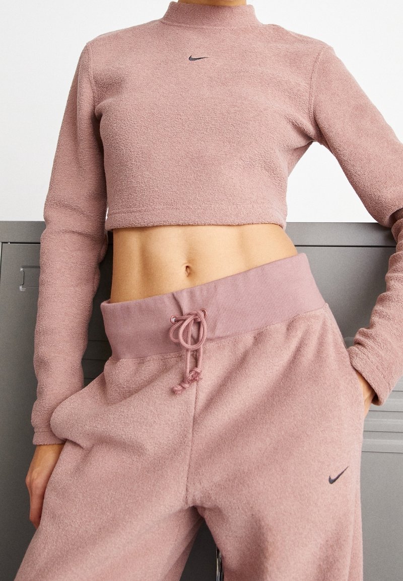 Nike rosa kortärmad sweatshirt med långa ärmar och hög halsringning, kombinerad med matchande sweatpants med elastisk midja och snörning.