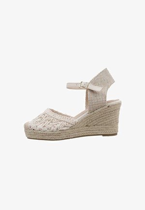 Sandalia de cuña con parte superior de tejido trenzado, color beige claro y correa en el tobillo. Suela de esparto con textura de cuerda y detalles de bordado intrincado.