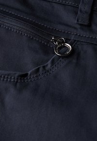 Tejido azul marino con un pequeño bolsillo con cremallera, un slider metálico y un acento de anillo circular. Textura suave y detalles de costura.