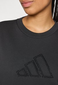 Mørk grå sweatshirt med rund hals, med et blankt, svart perlelogo design foran. Glatt, bomullsliknende tekstur.