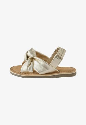 Child's gold metallic sandal with knotted front strap, cushioned tan footbed, and adjustable heel strap against white background.