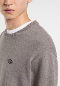 Maglione grigio a maglia con colletto a coste e un piccolo logo nero sul petto. Texture morbida e vestibilità standard con spalle rilassate.