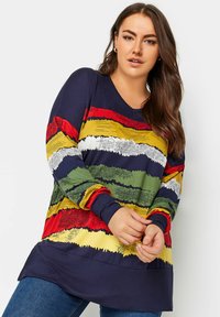 Monivärinen pitkähihainen paita, jossa on rohkeita raitoja punaisena, vihreänä, keltaisena ja laivastonsinisenä, V-kaula-aukko ja teksturoidut yksityiskohdat.