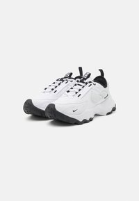 White sneakers with a textured black rubber sole, featuring a padded collar, black laces, and a Nike logo on the side and tongue.