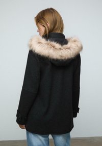 Čierny kabát s umelou kožušinou na kapucni, s voľným strihom a gombíkovými manžetami. Nosený cez svetlomodré džínsy.