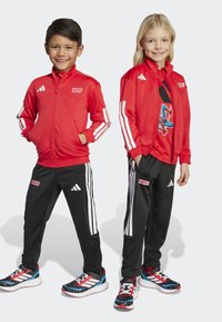 Rode sportjacks met witte strepen en 'Marvel'-logo's, gecombineerd met zwarte broeken met witte zijstrepen en sneakers met rode accenten.