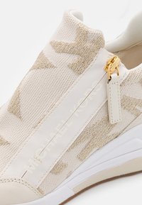 Baskets beige Michael Kors avec motif en maille métallique dorée, garniture en cuir blanc et fermeture éclair dorée avec tirette sur le côté.