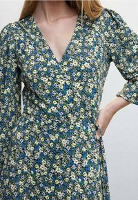 Blumenkleid mit tiefem V-Ausschnitt, dreiviertelÄrmeln und einer Mischung aus blauen, grünen und weißen Blumen auf dunklem Hintergrund.