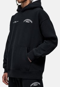 Felpa nera con cappuccio, tasca frontale, e polsini e orlo a costine. Presenta un logo in testo bianco sul petto e sulla spalla sinistra. Tessuto morbido e strutturato.