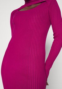 Gros plan sur une personne portant une robe ajustée à manches longues côtelée de couleur magenta avec un large décolleté dévoilant le haut de la poitrine et le cou.