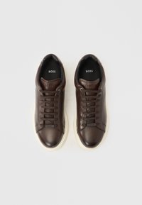Baskets en cuir marron à texture lisse, avec un bout arrondi et une semelle en caoutchouc blanche. Elles présentent des lacets ton sur ton et le logo "BOSS" sur la languette.