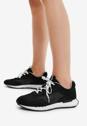 Baskets de sport noires avec des lacets blancs, dotées d'un dessus en maille et d'une semelle rembourrée. Le design comprend une semelle extérieure contrastante noire et blanche.