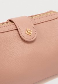 Ροζ δερμάτινο πορτοφόλι με χρυστό φερμουάρ και κλείσιμο με πατ, με χρυσή λεπτομέρεια λογότυπου και υφή στην επιφάνεια.