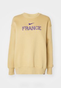 Beżowy sweter z okrągłym dekoltem z niebieskim logo Nike i haftowanym napisem "FRANCJA" na klatce piersiowej, posiadający długie rękawy oraz ściągacze na mankietach i u dołu.