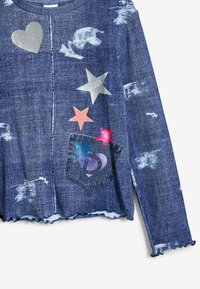 Džinsová blúzka s dlhým rukávom, ktorá má scalloped lem, aplikácie viacfarebných hviezd a srdiečok a predné vrecko s grafickými detailmi.