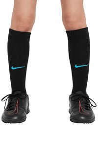 Crne čarape do koljena s rebrastim rubovima i tirkiznim Nike logotipom. Nosit će se s crnim nogometnim cipelama s crvenim akcentima i teksturiranom površinom.