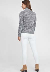 Stickad polotröja i en melerad grå nyans, kombinerad med vita jeans och bruna ankelskor med klack.