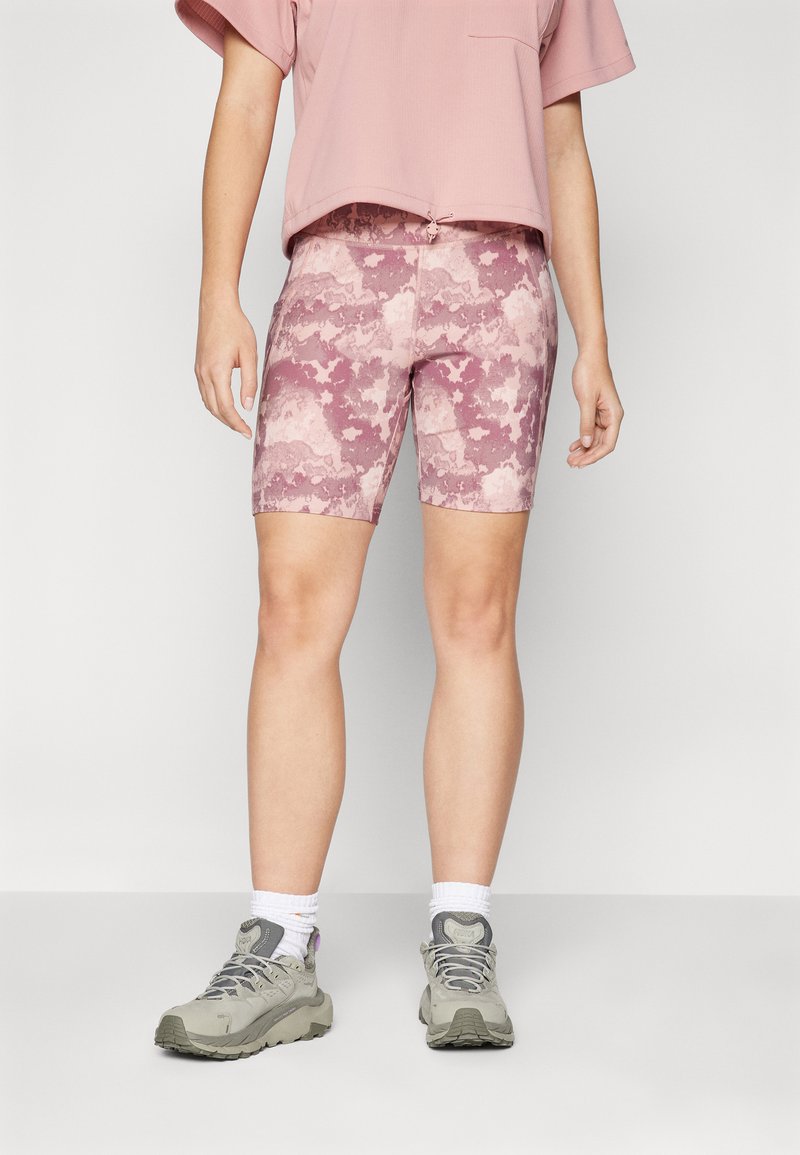 Rosa-mønstrede sykkelshorts i rosa nyanser, en avslappet passform rosa topp, og lyse grå tur-sko med hvite sokker. Strukturert stoff gjennomgående.