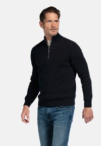 Schwarzer gerippter Pullover mit halbem Reißverschlusskragen, strukturiertem Stoff und langen Ärmeln. Kombiniert mit blauen Jeans für einen lässigen Look.