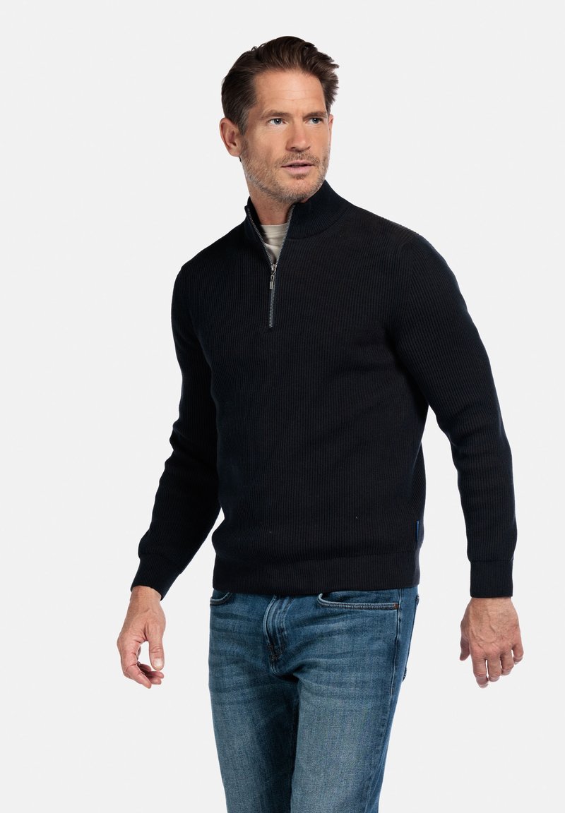 Schwarzer gerippter Pullover mit halbem Reißverschlusskragen, strukturiertem Stoff und langen Ärmeln. Kombiniert mit blauen Jeans für einen lässigen Look.