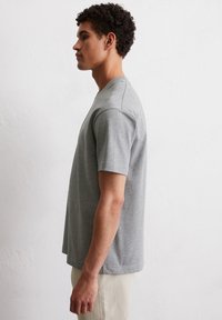 Szara bawełniana koszulka z krótkim rękawem, okrągłym dekoltem i luźnym krojem. Gładka struktura, prosty dół, minimalistyczny design.