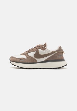 Baskets Nike blanches et beiges en suède et mesh, logo Swoosh marron, semelle blanche épaisse avec crampons noirs.