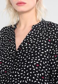 Blusa nera con un motivo geometrico di forme bianche e rosse, con leggero scollo a V e una texture del tessuto morbida.
