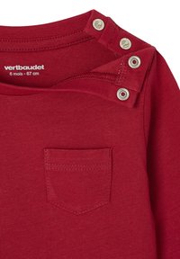 Rotes Langarmshirt mit Rundhalsausschnitt, ausgestattet mit Druckknöpfen an der linken Schulter und einer kleinen Brusttasche. Weicher Baumwollstoff.